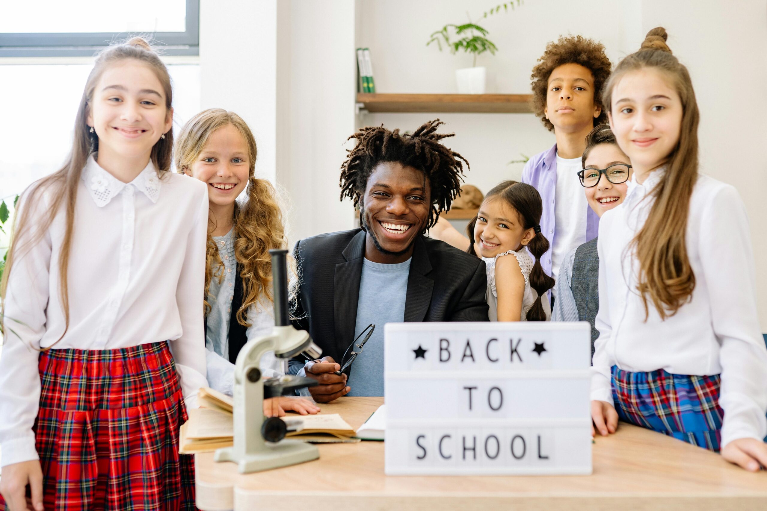 A diverse group of smiling students with their teacher in a classroom setting.